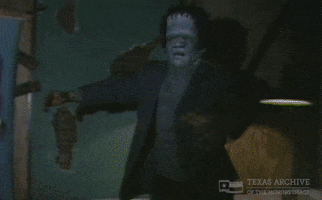 Video gif. Man wearing a Frankenstein mask holds his arms out for balance as he walks through a dark room like he's chasing someone. The video cuts to a low shot of feet walking upstairs away from us. 