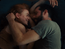 Movie gif. Sadie Sink as Her and Dylan O'Brien as Him in All Too Well lie facing each other as they caress each others faces with affection on a loop.