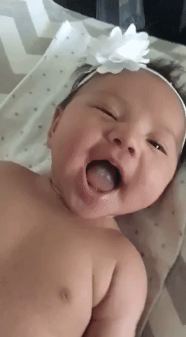 Video gif. A cute, dimpled baby with a bow on her head smiles at us and winks.