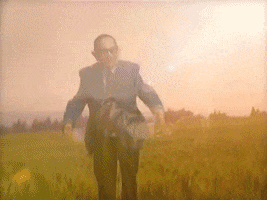 Music Video gif. Older man in suit with pointed elf ears runs, arms outstretched. Perspective fades to the person he's running to, a purple skinned, purple haired woman with pointed elf ears holding her large gold gown as she runs towards the man.