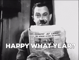 Video gif. Black and white footage of a man smoking a cigar with a confused expression as he looks at a newspaper. Text, "Happy what year?"