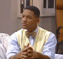 TV gif. Will Smith on The Fresh Prince of Bel-Air sits very still on the couch with his legs cross, and his hands together on his knee. He is dressed like Carlton, in preppy clothes and has round glasses on.