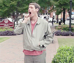 Movie gif. Jim Carrey as Lloyd in Dumb and Dumber To, stands on a sidewalk and attempts to spray breath freshener into his mouth in anticipation of a kiss. The spray is pointed the wrong way and a ploom goes out to the side of his wide open mouth. 