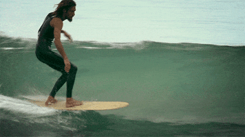 Sports gif. Surfer gracefully rides a curly wave and holds his arms out for balance.