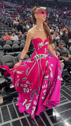Celebrity gif. Radmila Lolly spins in a circle, showing off  a pink dress made from her own jerseys and she wears matching pink sunglasses on the sidelines of a basketball game.