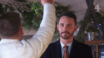 TV gif. Gregory Finnegan as James in Hollyoaks looks amused while Kieron Richardson as Ste holds mistletoe above them with his lips puckered up for a kiss.