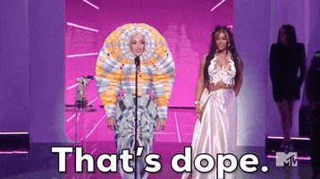 Celebrity gif. Doja Cat and Sza stand at the podium for the 2021 VMAs and Doja accepts an award in a maximalist worm-like outfit.