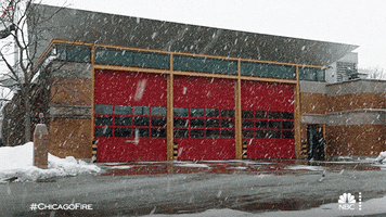 TV gif. In a scene from Chicago fire, heavy snow falls continuously at a diagonal around a fire station.