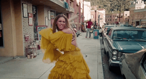 An animated gif that's a clip from the Beyonce Lemonade video where she is wearing a yellow dress and smashing a car window with a bat