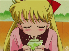 Cartoon gif. Minako from Sailor Moon leans over a table, holding a green drink and blowing bubbles through the straw.