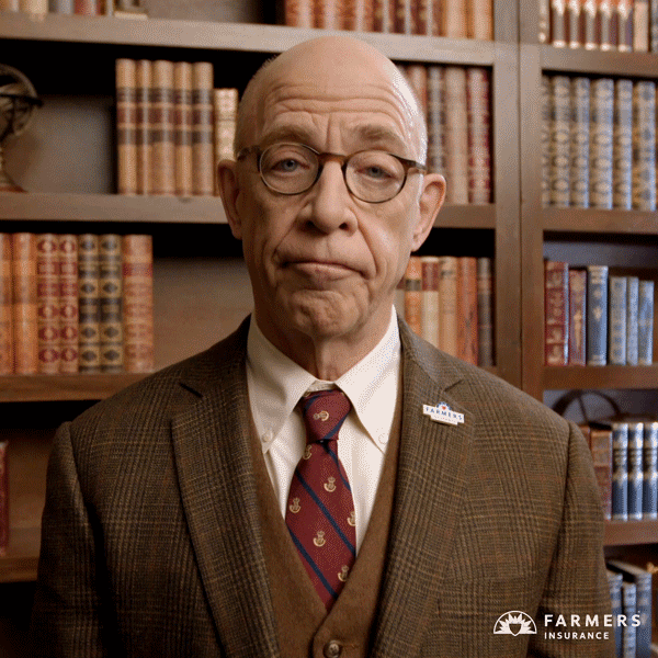 Ad gif. JK Simmons stands in front of an old-looking bookshelf, wearing a brown suit jacket, a red tie, and a small "Farmers Insurance" pin. He shrugs at us, then gently nods.
