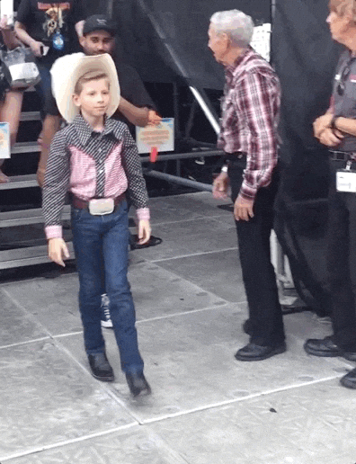 Video gif. A child dressed like a cowboy does a flashy 360 spin and points finger guns to one side.