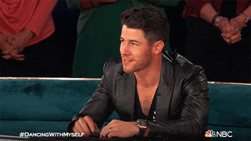 Reality TV gif. Nick Jonas in Dancing with Myself. He shakes his head slightly and waves his hand to say no, while tilting his head and smiling with strain.
