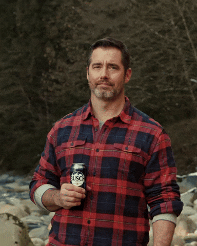Video gif. A man wearing a red flannel holding a Busch beer holds up his pointer finger and shakes it around as if to say “no way.”