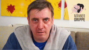 Video gif. Looking miserable, a man suffering from the man flu sits on his couch and gives us two thumbs up.