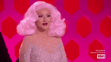 TV gif. Christina Aguilera on RuPaul's Drag Race is all done up with voluminous light pink hair. She bends forward and laughs daintily.