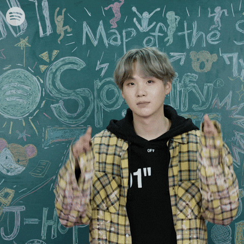 Celebrity gif. Suga from BTS stands in front of a Spotify chalkboard and gives two thumbs up.