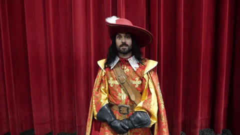 Gif of a man dressed as a musketeer in front of a red velvet curtain taking a bow.