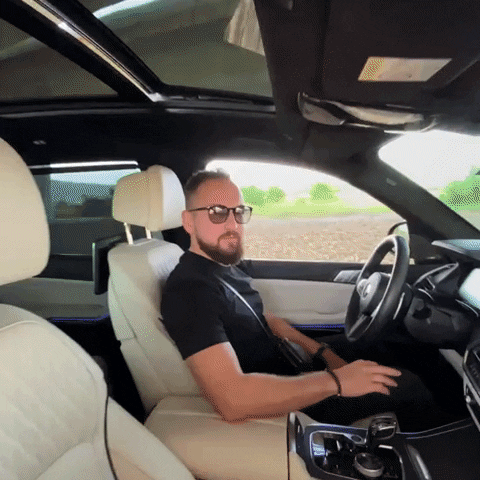 Video gif. A man, sitting in the driver's seat of a car, gives a knowing head shake, a smile, and a thumbs up. 