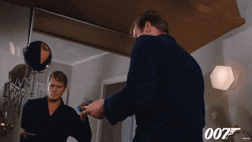 Movie gif. Roger Moore as James Bond in Live and Let Die spins around, facing us, holding a cigar end up to a blue aerosol can, causing the can to spew flames.