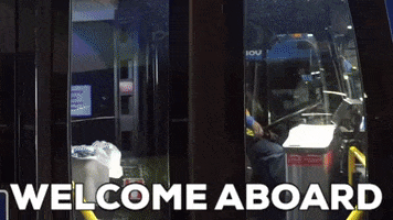 Video gif. A bus driver opens the glass double doors of a city bus and waves warmly at us. Text, "Welcome aboard."