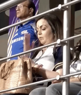 Celebrity gif. Nita Ambani sits in the bleachers of a cricket game with her purse on her lap. She has her eyes closed and her head slightly bowed as she mutters a prayer to herself. She points to different parts of her face such as points on her forehead, her eyes, and then points to her chest.