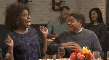 SNL gif. Sitting at a table, happy Leslie Jones gives Kenan Thompson an excited high five.