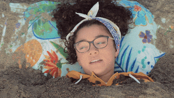 TV gif. Malia Baker as Mary Anne in Babysitters Club lies buried up to her neck in sand and says, “I'm literally in too deep.”