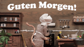 Cartoon gif. Stop motion brown felt mouse wearing a chef's hat and an apron pulls a tray of muffins out of the wood stove, tilting is head back as it takes in the aroma of the freshly baked muffins. Text, "Guten Morgen."