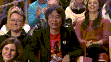 Celebrity gif. Shigeru Miyamoto sits in the stands with a crowd of people and frowns, giving a thumbs down. Then he slowly turns his hand to a thumbs up with a laugh as he says, "Good job."