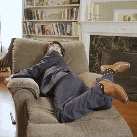 Video gif. A tired man flops pathetically onto a chair, slumping over. Text, “Mondays…”