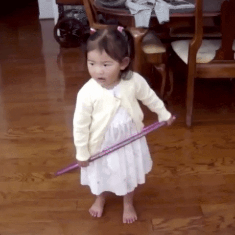 Video gif. A cute girl wearing a white dress with pigtails in her hair attempts to hula hoop but fails. As the hula hoop lies on the ground, she continues to wiggle back and forth as if she is hula hooping.