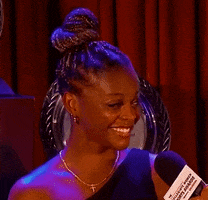 Video gif. Gymnast Trinity Thomas grins and gives us a cheeky winks after answering a question from an interviewer at an awards ceremony.