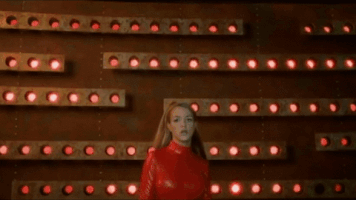 Music video gif. Britney Spears wearing a red bodysuit in the Oops I Did It Again video, walks towards us in bold defiance, reaching out and grabbing right at our face as she sings, "Oops I did it again!"