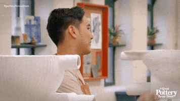 Reality TV gif. Man from the Great Pottery Throw Down smiles and applauds someone in a room surrounded by handmade white clay pots.