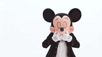 Disney gif. Mickey Mouse is giggling in the corner and he has his paws up to his lips before blowing us a big kiss.