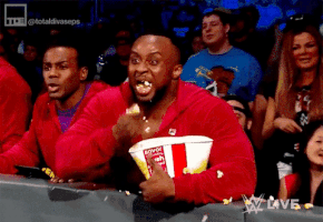 TV gif. A captivated WWE fan excitedly chomps popcorn, making a mess.