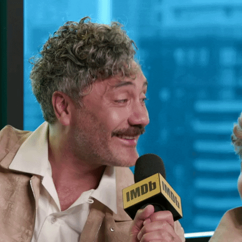 Celebrity gif. Taika Waititi leans into a microphone and nods in agreement, laughing and smiling as he speaks into the mic. He says, ‘You're right.”