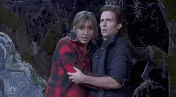 SNL gif. Man holds a scared woman in a graveyard, as they both look around in terror.