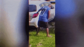 Video gif. A man staggers forward, trying to grab onto the side of a car. He then leans over too far and ends up falling down on his stomach. The video is glitching. 