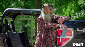 Reality TV gif. Si Robertson on Duck Dynasty leans on the tailgate of a truck with one foot up on the bumper as he laughs hard, leaning forward a little. 