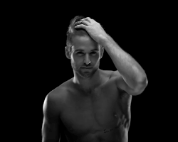 Video gif. A black and white video of a muscular, shirtless man with a thin beard, smirking and running a hand through his hair. We then see him from the back as he turns around to face us.