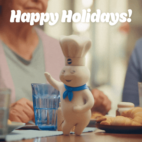 Sponsored gif. The Pillsbury Doughboy, in his iconic blue scarf and Pillsbury chef hat, dances on a holiday table. We can see a family eating crescent rolls in the background. Text: "Happy Holidays!"