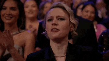 Oscars 2024 GIF. Kate McKinnon, at the Oscars, steely tries to reign in her emotion as she applauds.