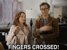 Movie gif. Kimberly Williams-Paisley as Claire and Tom Cavanagh as Miles in Darrow and Darrow turn toward each other with their fingers crossed and say, "Fingers crossed!"