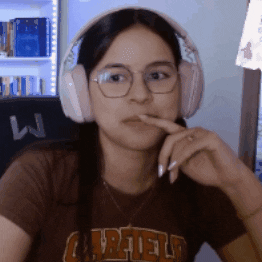 Video gif. A woman wearing headphones and glasses looks at us with wide eyes and a shocked expression on her face. She covers her mouth with her hand.