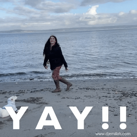 Video gif. As her little dog watches, Influencer Djamilah Burnie jumps on the beach, flinging her arms into the air as sparkles pop around her. Text, “YAY!”