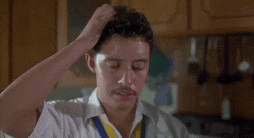 Movie gif. Efren Ramirez as Pedro in Napoleon Dynamite. He's standing in a house and is sweating heavily. He scratches his head and wipes his sweat, frowning down at something.