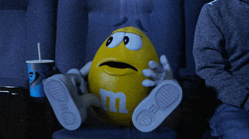 Ad gif. A yellow M&M looks around in fear and leaps out of their seat in the theater saying, "I'm out!"