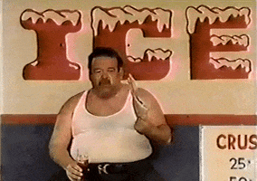 Video gif. Man is sitting in front of an ice sign holding a soda and is fanning himself with a pamphlet, trying to beat the heat.